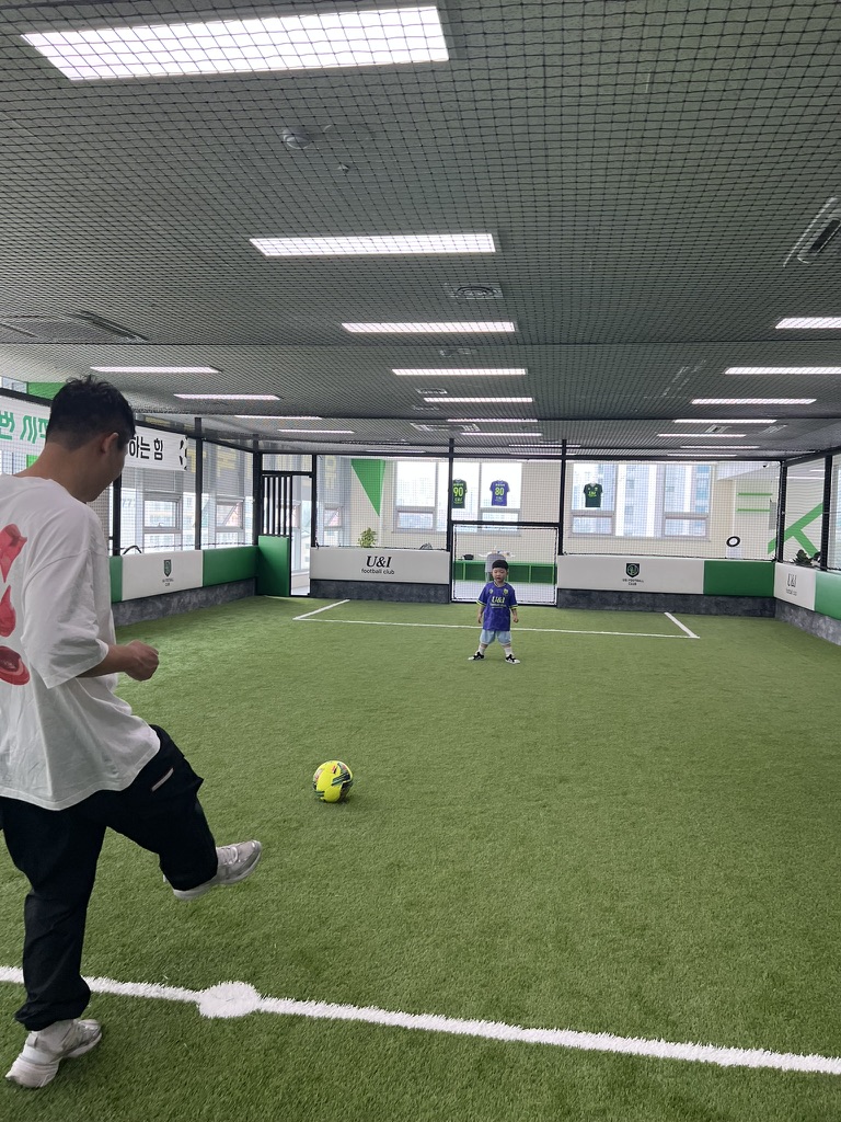 가을 햇살이 내리쬐는 공원 잔디밭에서 아빠와 5세 아들이 축구공을 주고받으며 활짝 웃고 있는 에너지 넘치는 모습
