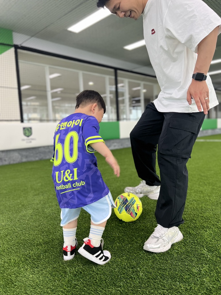 슛을 성공시킨 아들이 환하게 웃으며 두 팔을 벌리자, 아빠가 무릎을 굽히고 아들을 따뜻하게 안아주며 칭찬하는 감동적인 순간